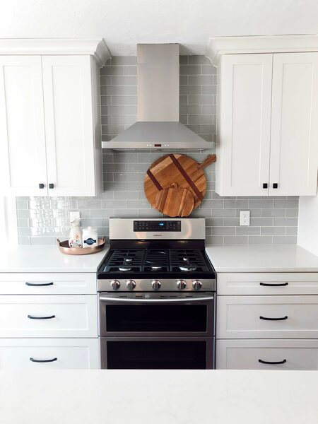  Modern kitchen with hood, stove, and white cabinets with knobs