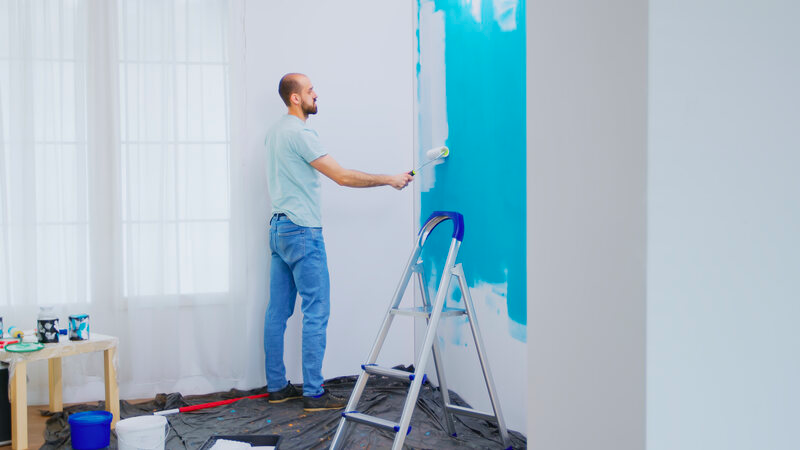 Man painting blue wall white with roller
