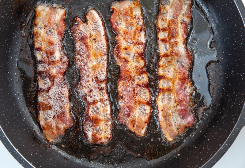 bacon sizzling in a pan in their grease