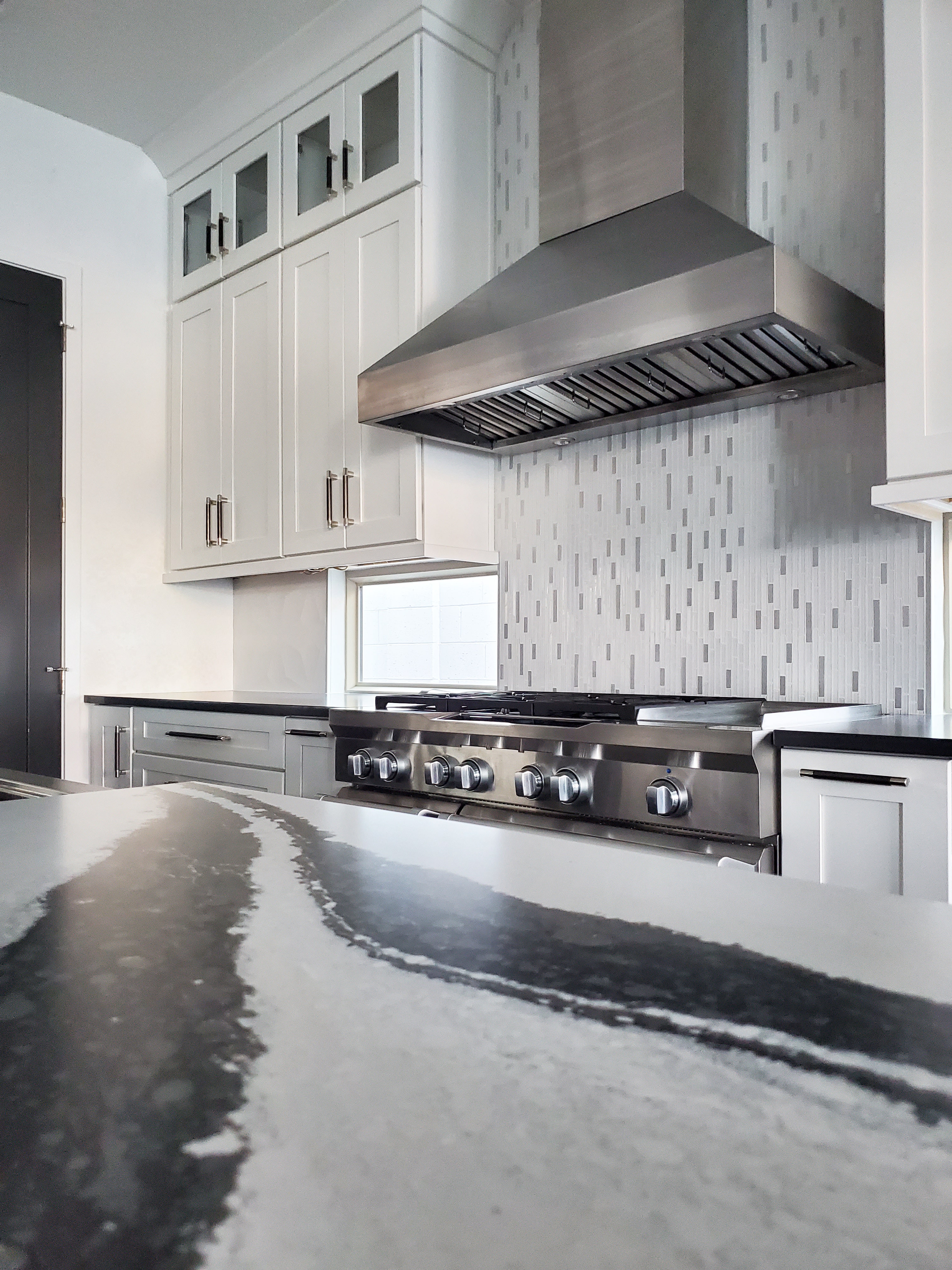 Sleek wall range hood with hidden buttons. Marbled counters and tiled backsplash. 