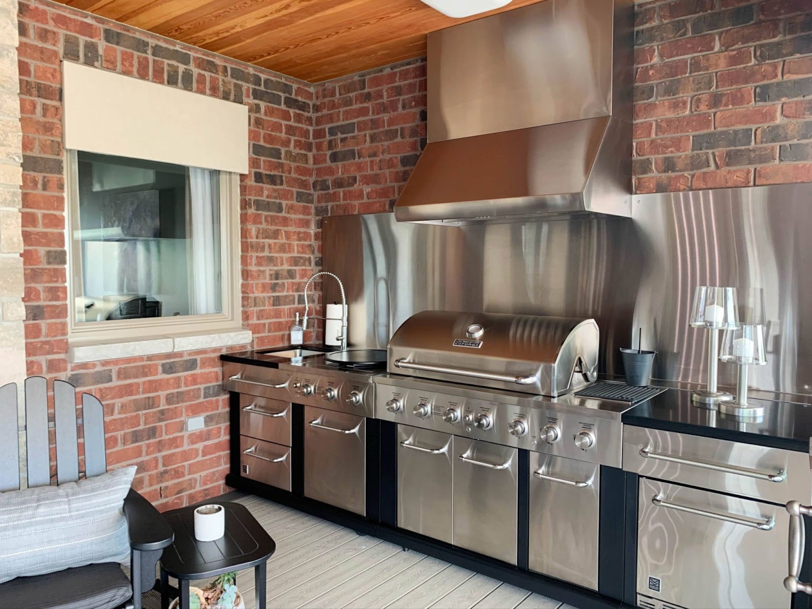 Indoor Grilling Nook: Exposed brick, wood celing, and Proline hood create a cozy grilling space with industrial-rustic vibes. Stainless steel accents and natural light add a touch of elegance. - Proline Range Hoods - prolinerangehoods.com 
