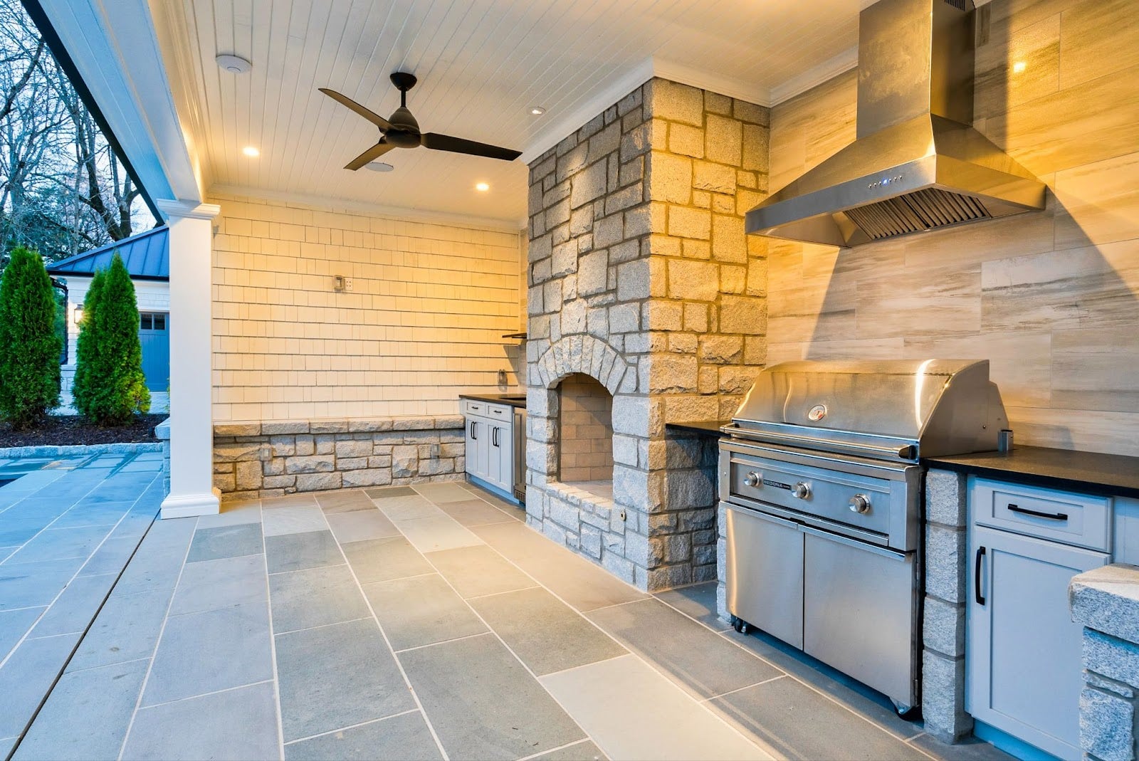 Seamless Outdoor Entertaining: Sleek Proline hood vents smoke while you cook by the pool in this inviting outdoor kitchen. Stone and stainless steel create a cohesive look, perfect for gatherings under the open sky. - Proline Range Hoods - prolinerangehoods.com 