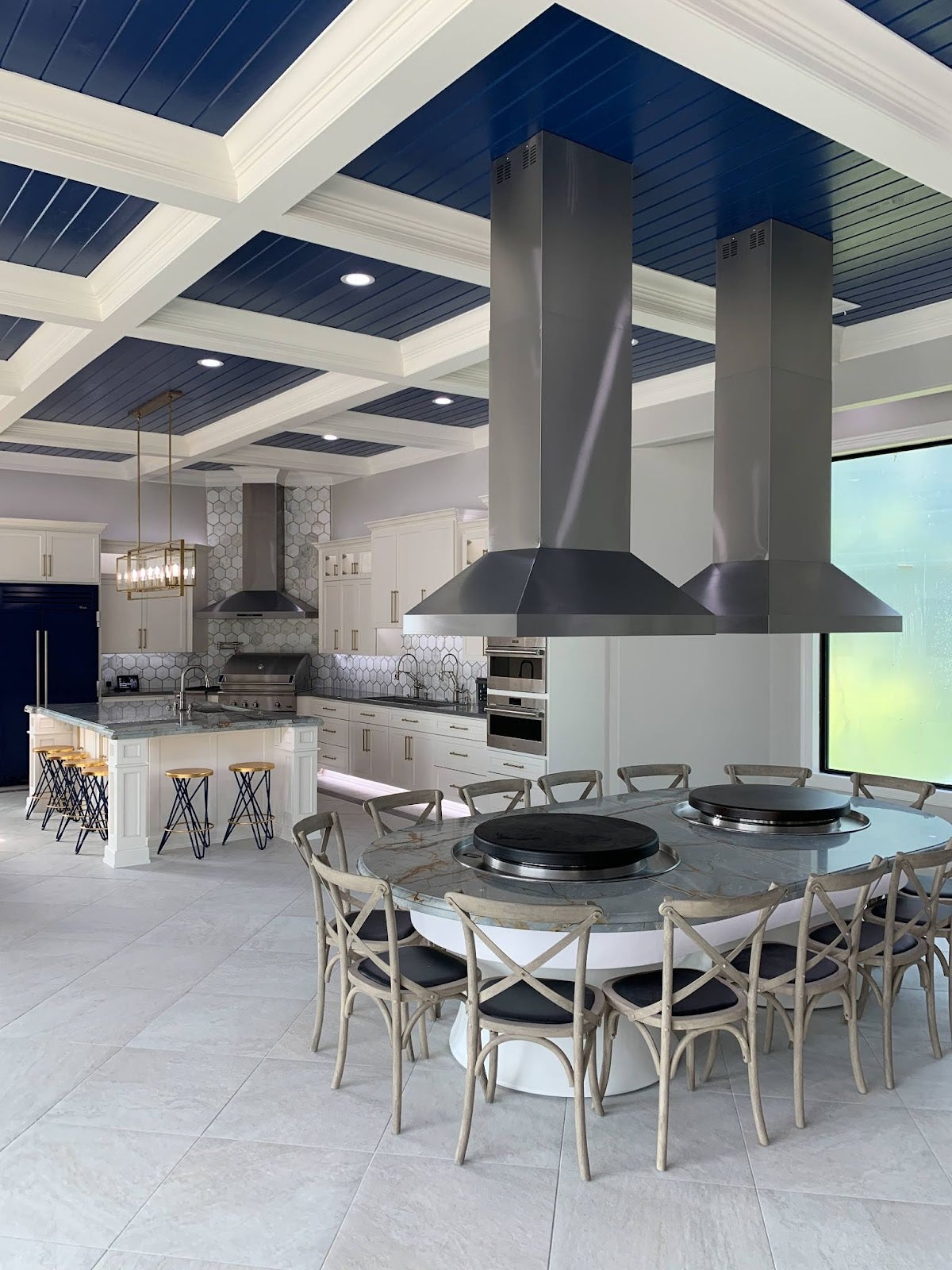 Coastal Luxe Outdoor Kitchen: Three Proline hoods vent smoke in this stunning outdoor kitchen. Blue and white color scheme creates a fresh vibe. Architectural ceiling adds a touch of luxury. Perfect for social gatherings and serious cooking. - Proline Range Hoods - prolinerangehoods.com 