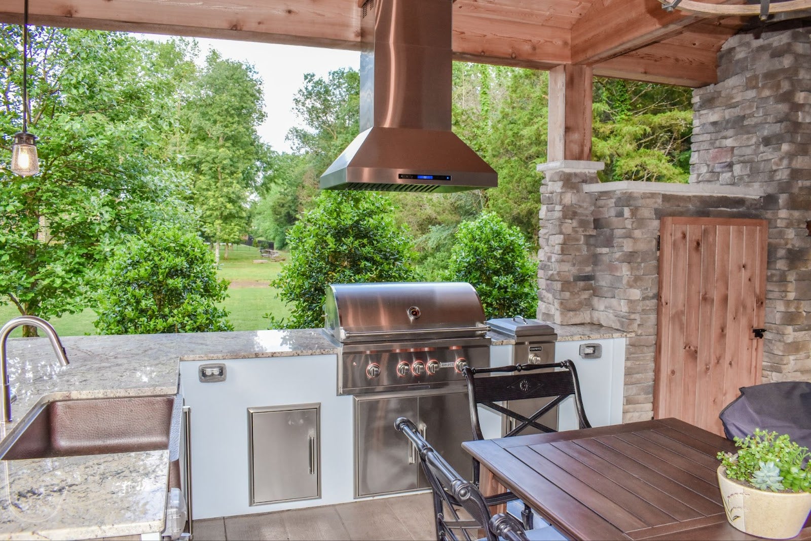 Rustic Meets Modern Grilling: Copper Proline hood adds style and function to this outdoor kitchen. Natural materials and a garden view create a serene space for gourmet grilling. - Proline Range Hoods - prolinerangehoods.com 