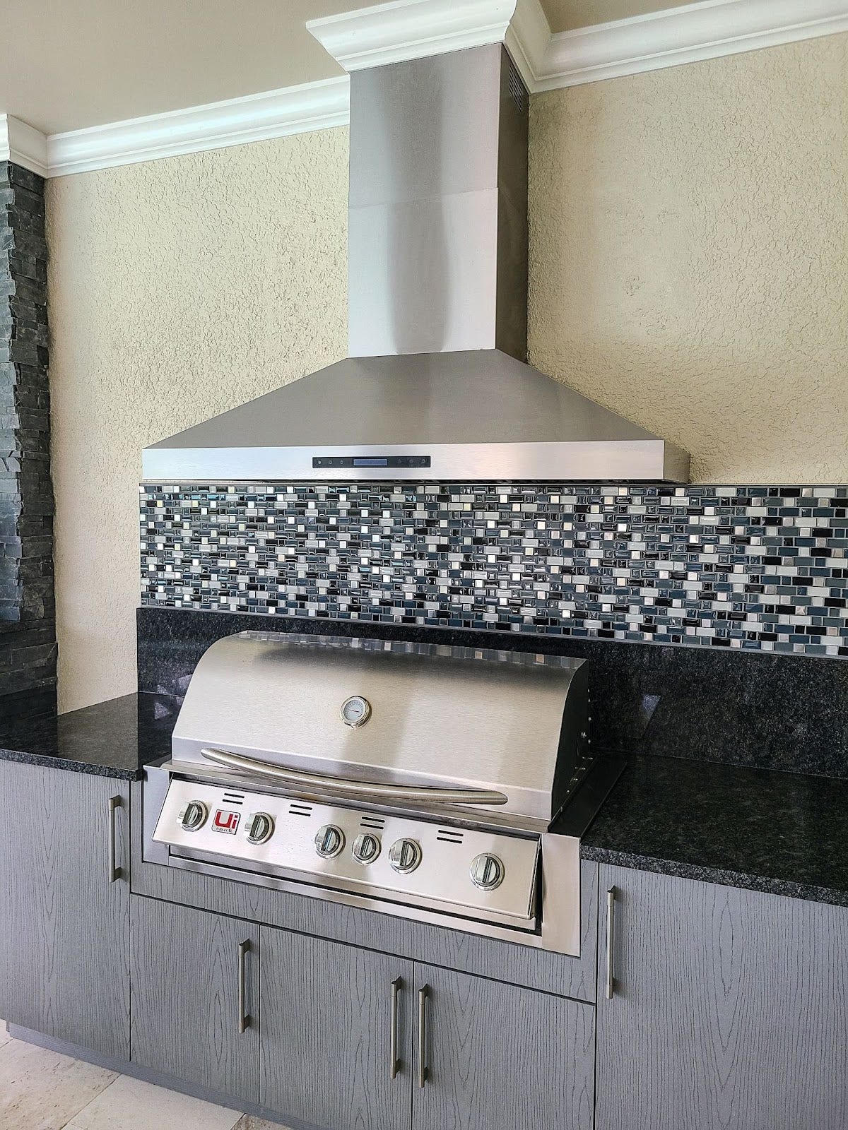 Modern Outdoor Kitchen with Mosaic Backsplash: Proline hood vents smoke in this stylish outdoor kitchen. Mosaic tile backsplash adds a pop of color. Perfect for grilling and entertaining with a modern feel. - Proline Range Hoods - prolinerangehoods.com 