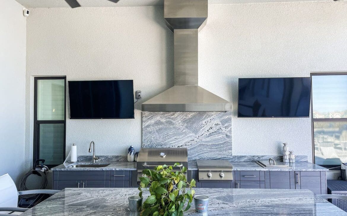 Modern Black & White Kitchen: Proline PLJI 104 hood stands out in this stylish outdoor kitchen with black and white marble and twin TVs. Chic fan adds a touch of elegance. Perfect for entertaining and enjoying the outdoors. - Proline Range Hoods - prolinerangehoods.com 