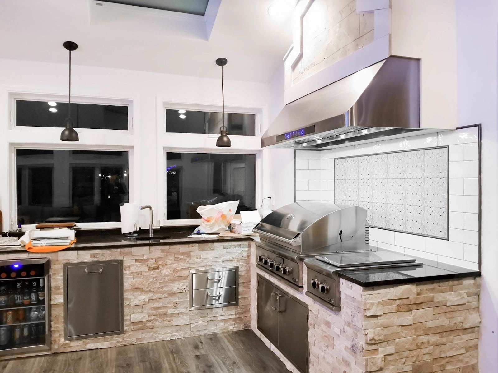 Fun Indoor/Outdoor Kitchen: This inviting kitchen features stone counters, stainless steel appliances, and a spacious grill. The Proline range hood keeps the air clear. A wine fridge and subway tile backsplash add stylish touches. Perfect for family gatherings! - Proline Range Hoods - prolinerangehoods.com 