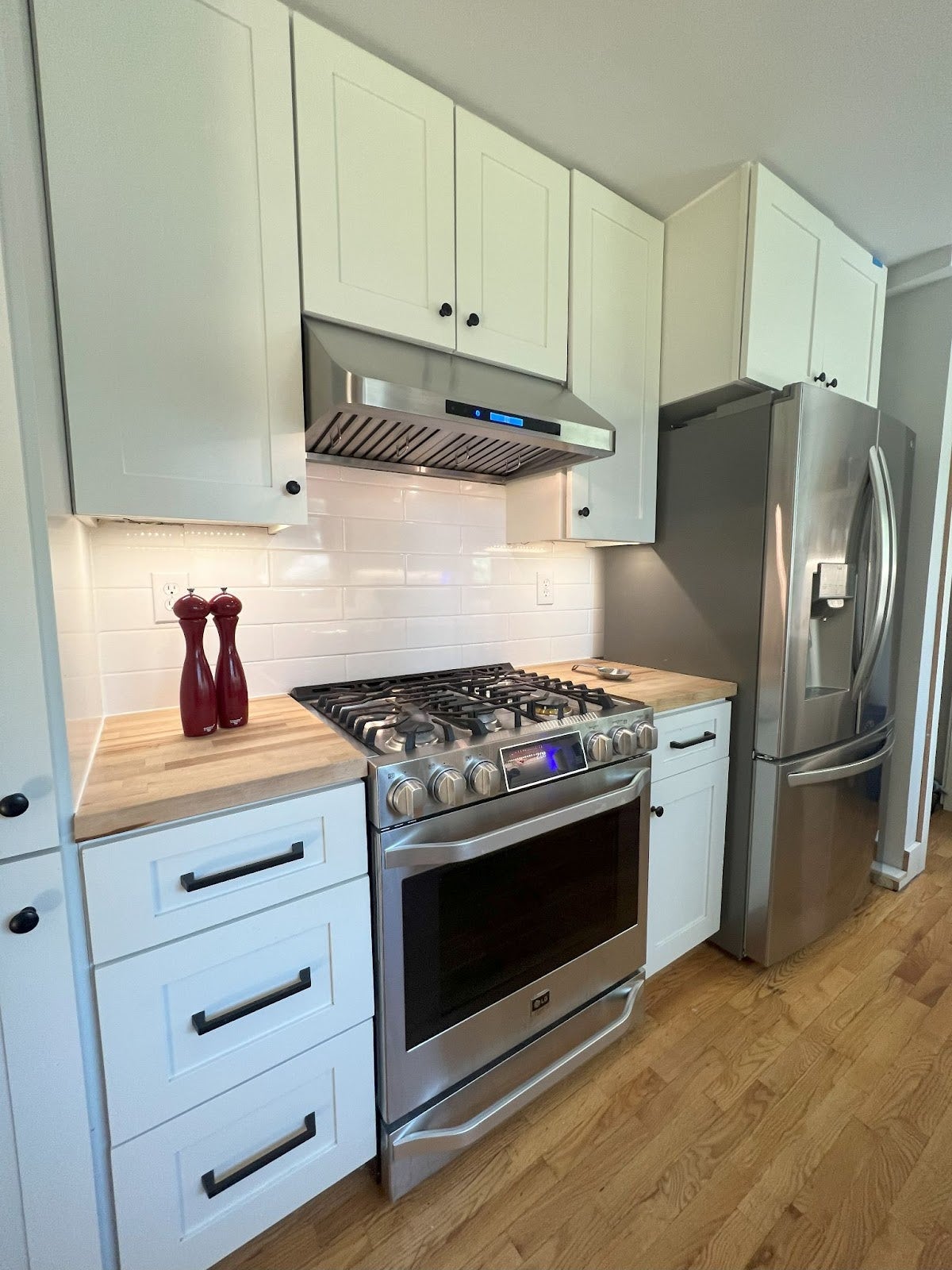 A stainless steel refrigerator and stove with sleek counter tops in a modern kitchen. - Proline Range Hoods - prolinerangehoods.com 