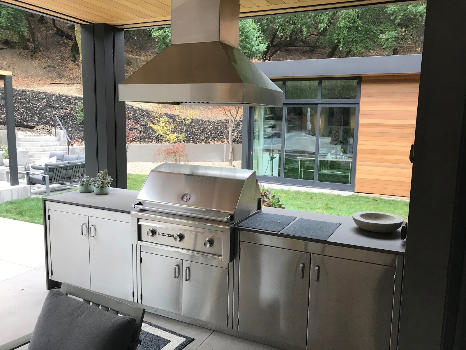 Sleek patio cooking space with a professional grill setup, overlooking a contemporary outdoor seating area and landscaped garden. - Proline Range Hoods - prolinerangehoods.com 