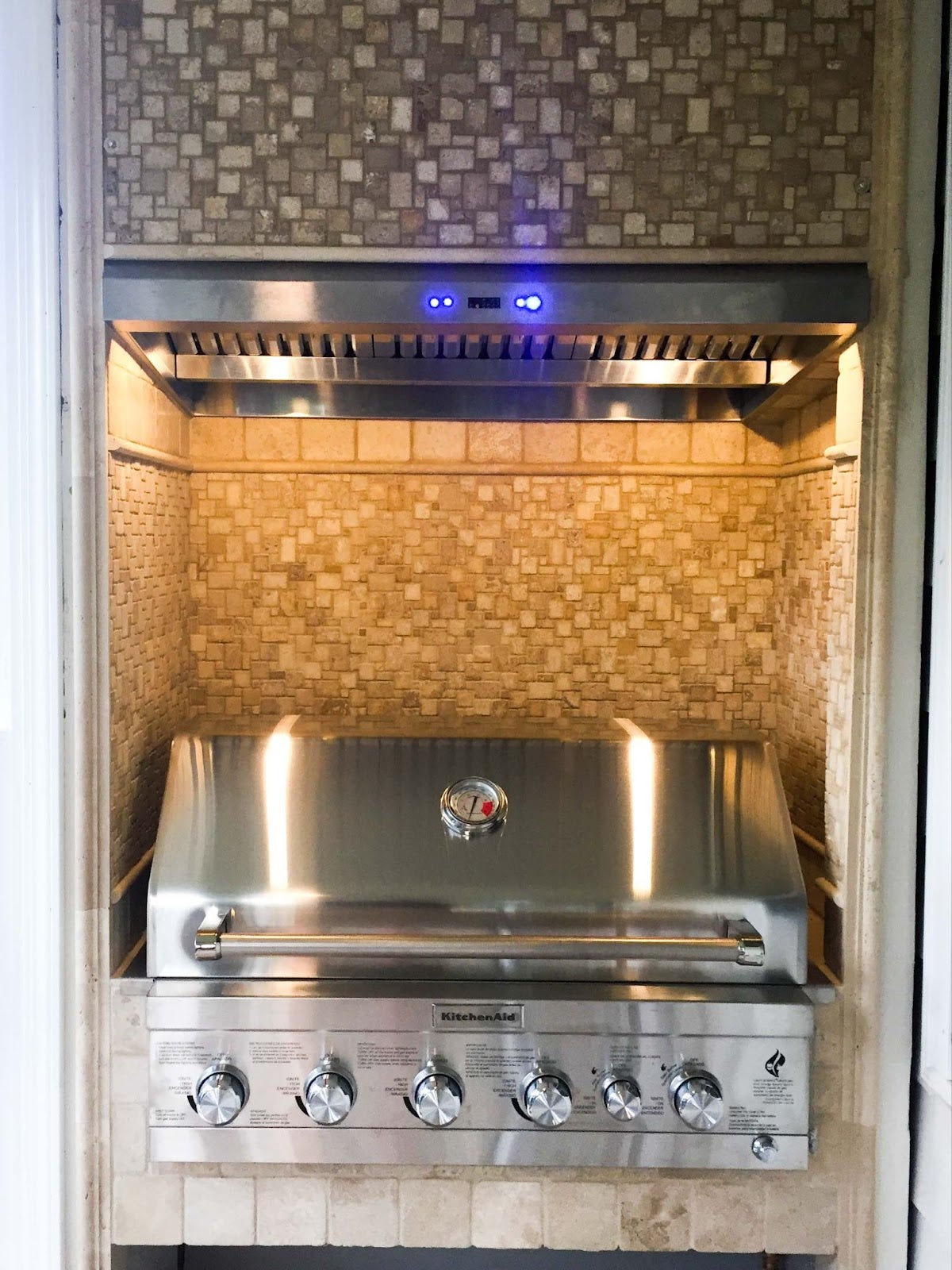 Elegant indoor grilling station featuring a Proline range hood with illuminated controls, complemented by a tumbled stone backsplash - prolinerangehoods.com