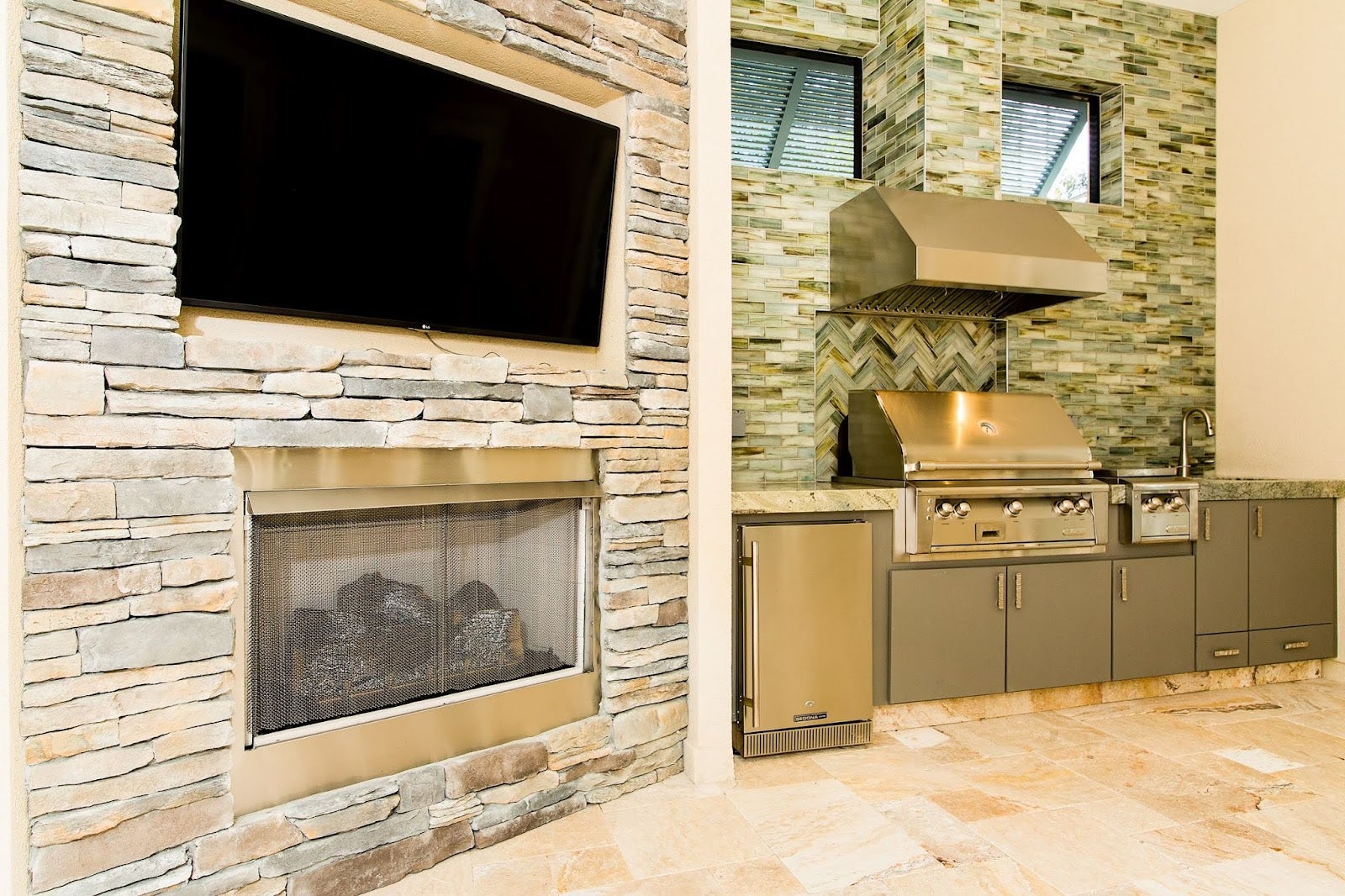 Elegant stone patio featuring a Proline range hood above a high-end grill, complete with sleek storage solutions and a mounted TV for entertainment - prolinerangehoods.com.