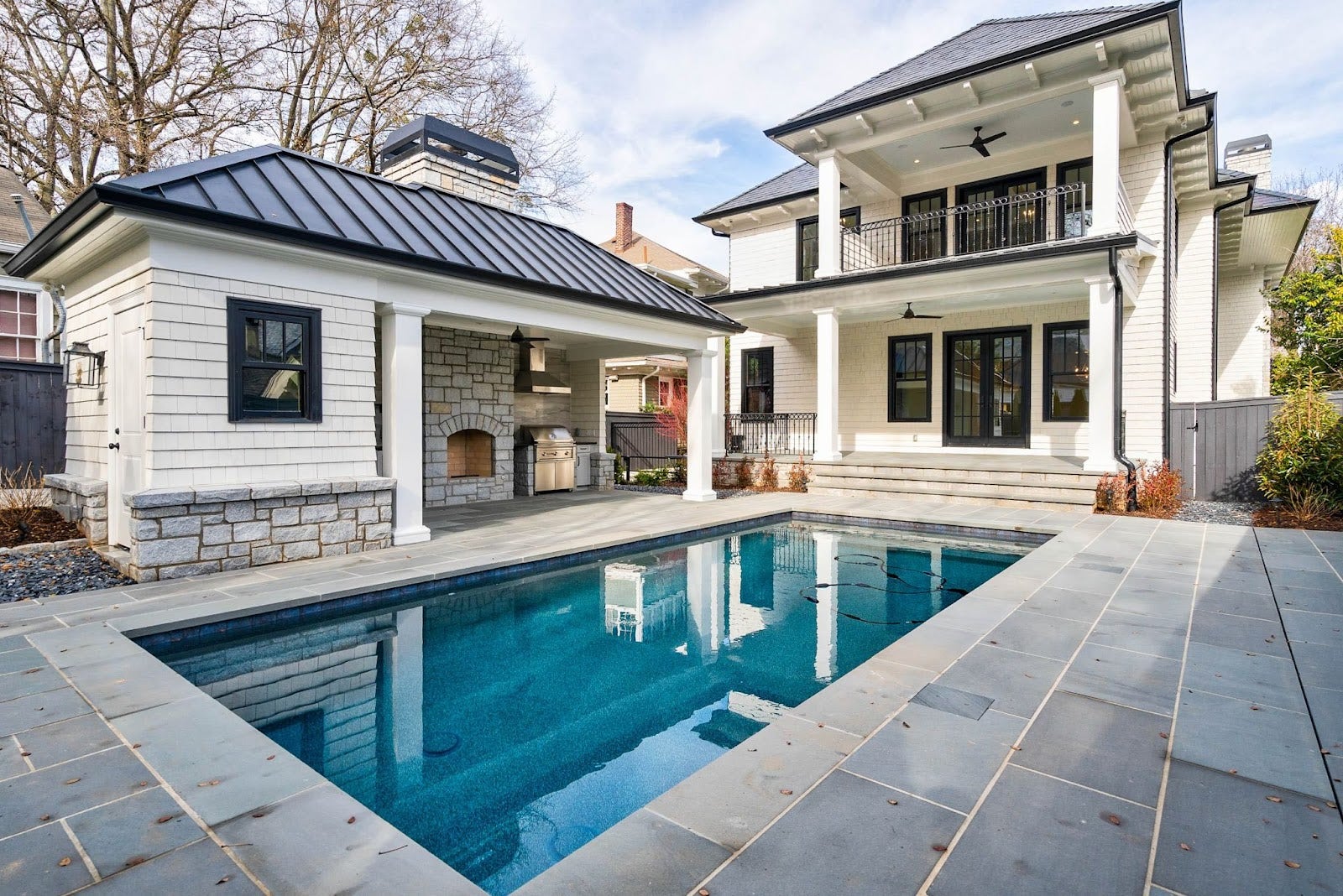 Elegant backyard retreat featuring a pristine pool, a cozy outdoor kitchen with a Proline range hood, and a classic fireplace, ideal for luxury living - prolinerangehoods.com.