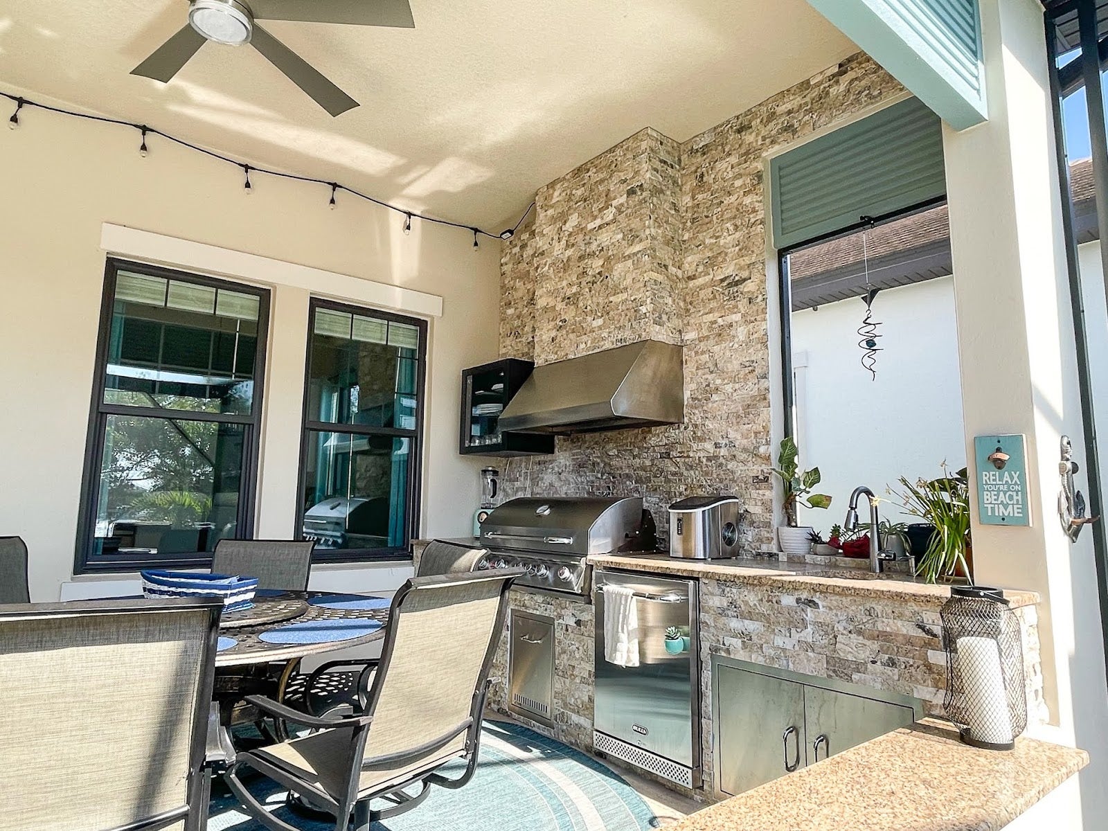 Proline range hood in an outdoor kitchen with stone finishes, including dining space and a relaxing 'beach time' sign - prolinerangehoods.com