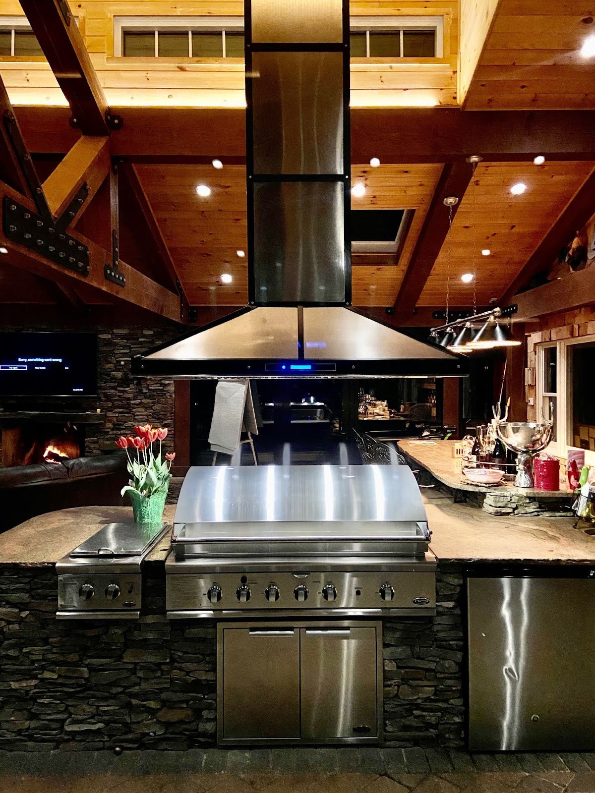 Proline range hood in a rustic stone outdoor kitchen with warm lighting and wooden accents - prolinerangehoods.com