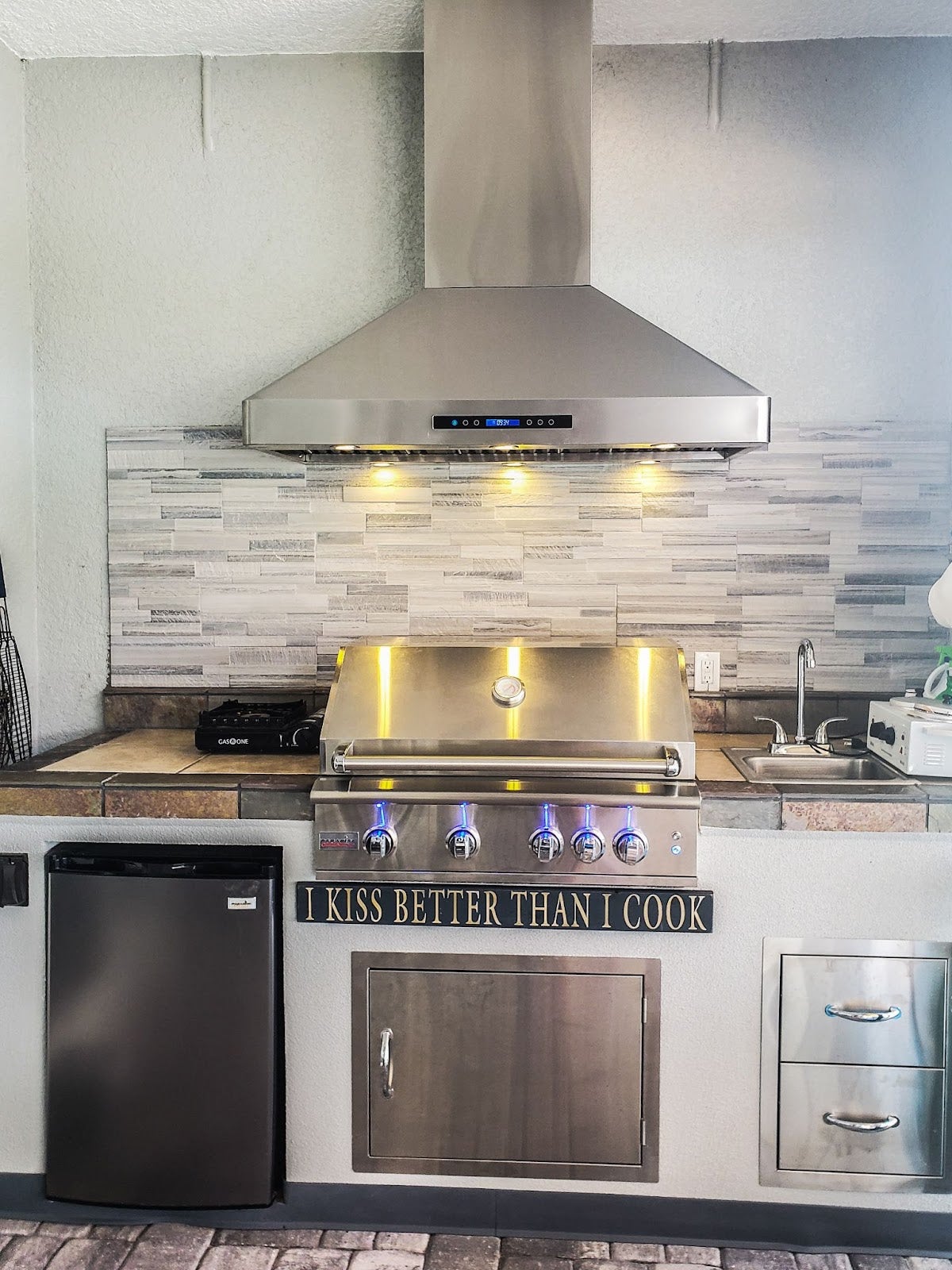 Stylish kitchen setup featuring a Proline range hood, LED-lit grill, and a humorous culinary quote, combining function with a touch of personality - prolinerangehoods.com.