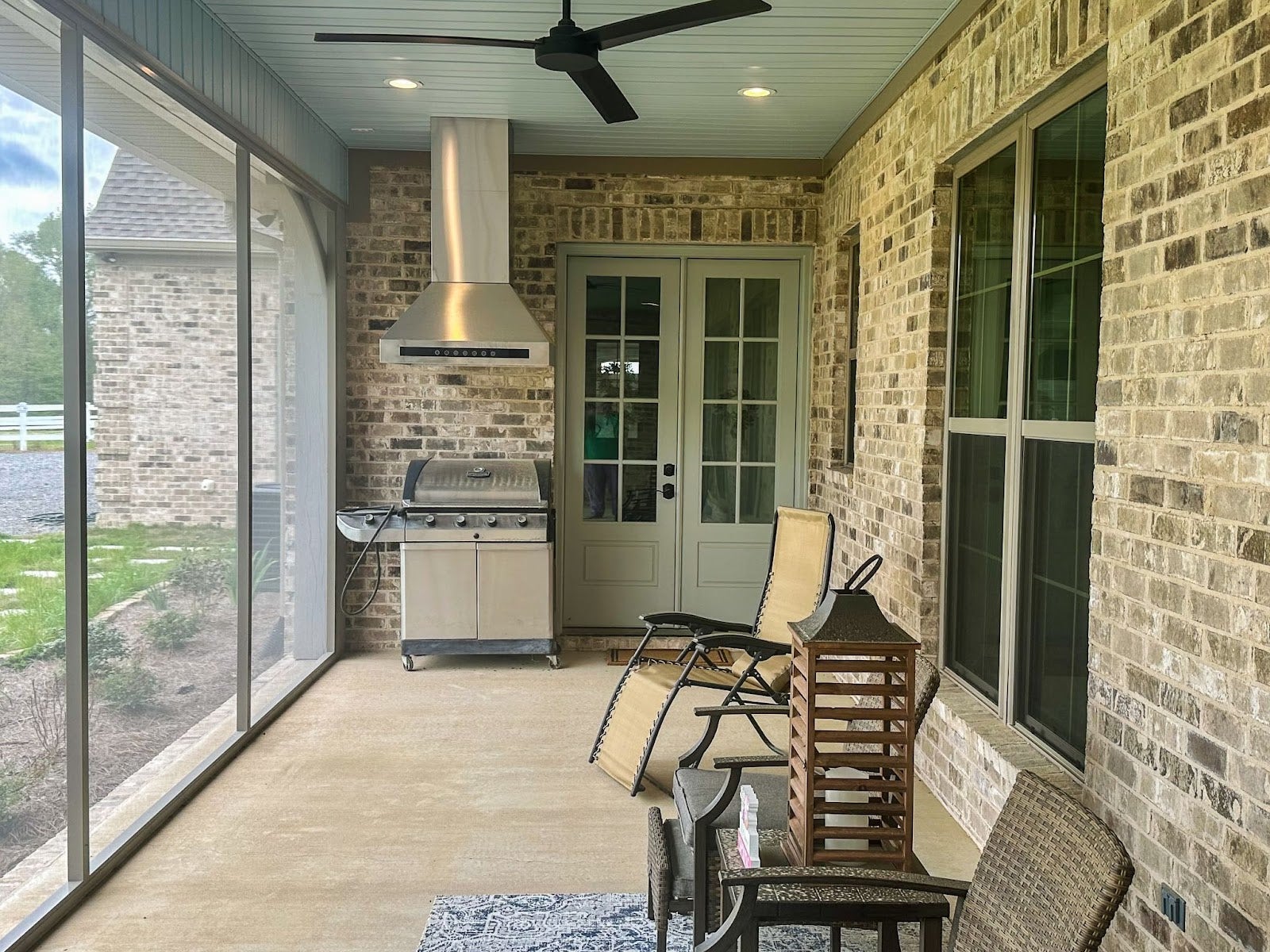 Covered patio with a stainless steel grill under a Proline wall range hood, surrounded by traditional brick walls and outdoor furniture - prolinerangehoods.com
