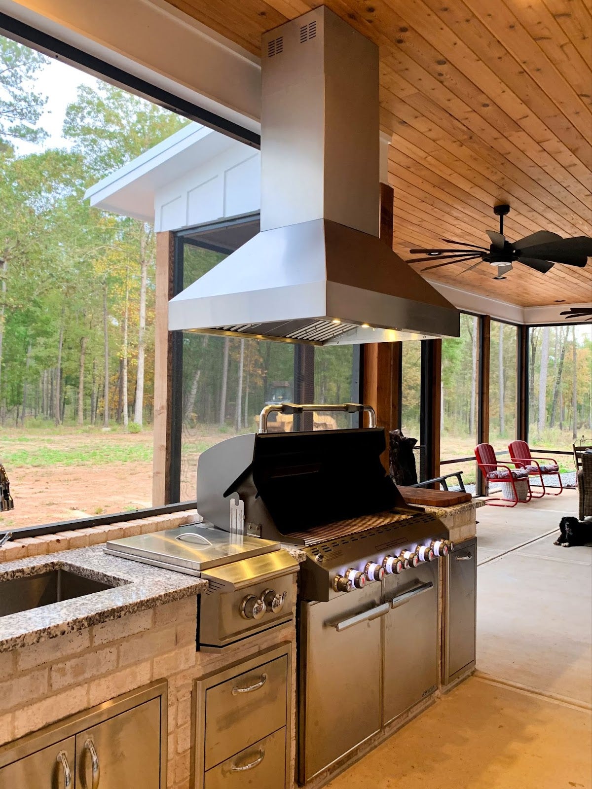 Spacious covered outdoor kitchen featuring a Proline range hood with a view into the woods - prolinerangehoods.com