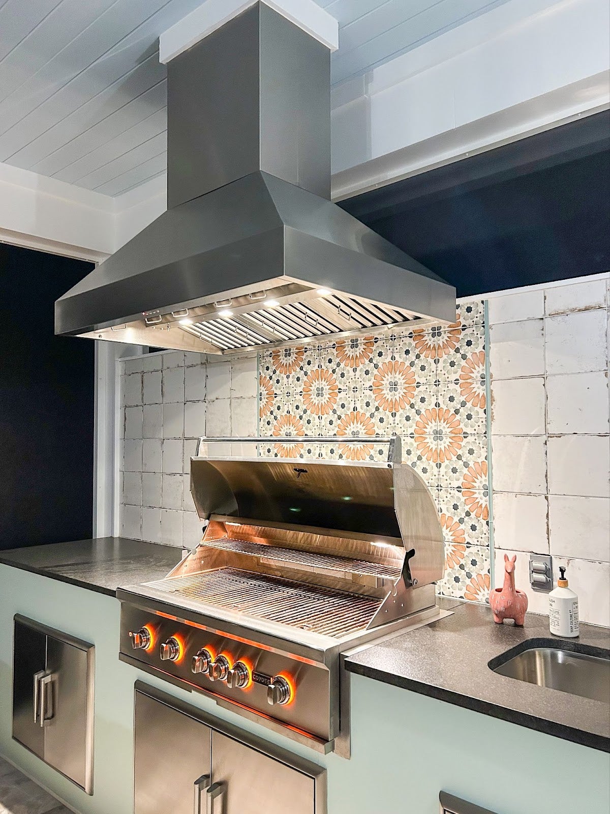 Stylish gourmet kitchen featuring a professional stainless steel grill and a colorful tile wall design. - Proline Range Hoods - prolinerangehoods.com 