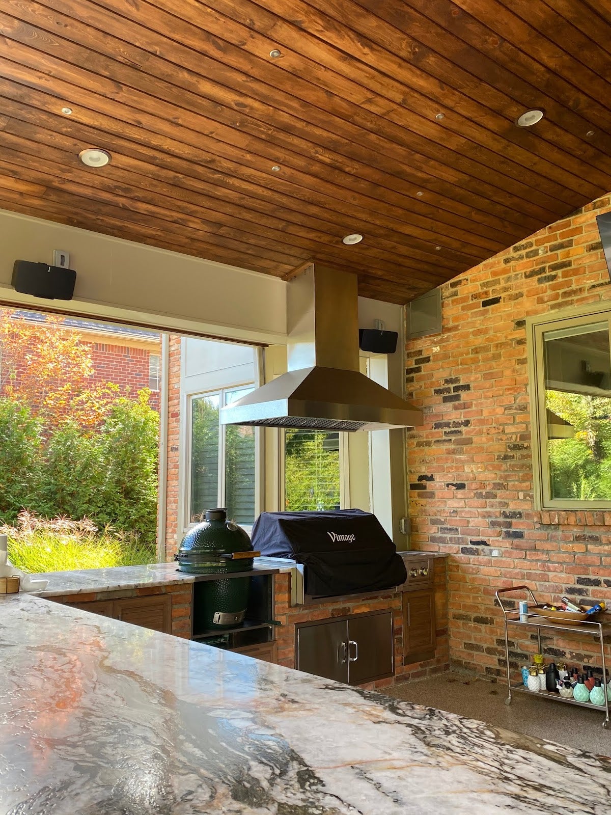 Elegant outdoor cooking space with a Proline range hood, brick accents, and wood plank ceiling - prolinerangehoods.com