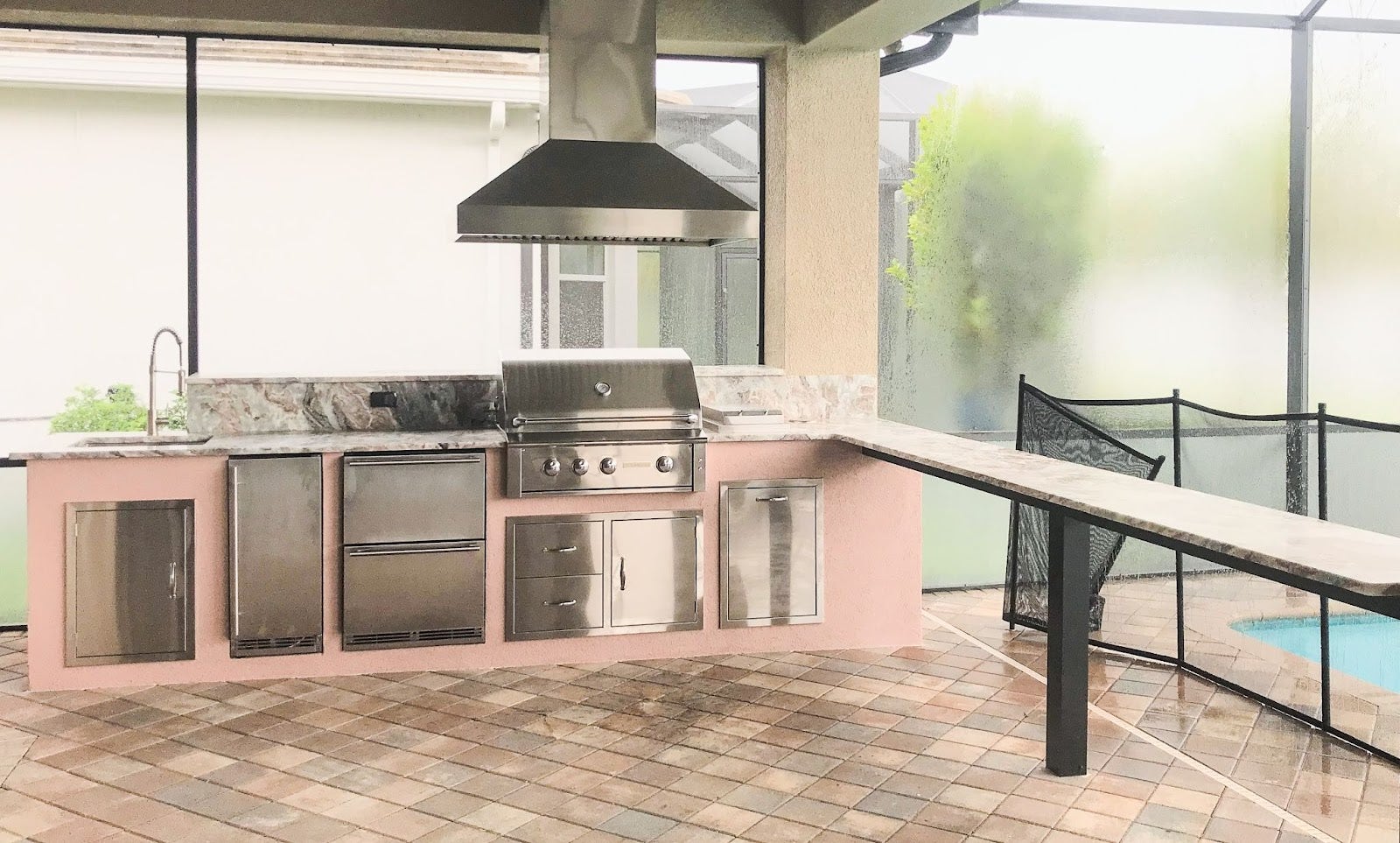 Contemporary outdoor kitchen with Proline range hood in a screened lanai with poolside view - prolinerangehoods.com
