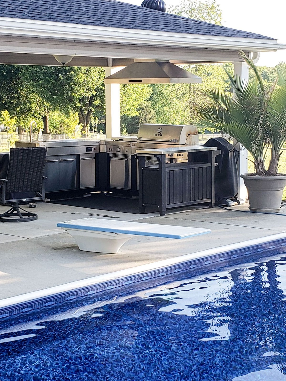 Relaxing outdoor cooking space featuring a Proline range hood by a tranquil swimming pool - prolinerangehoods.com