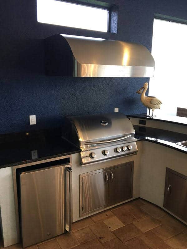 Stylish home grill station with a shining Proline range hood, contrasting beautifully with a vibrant blue wall and decorative bird sculpture - prolinerangehoods.com.