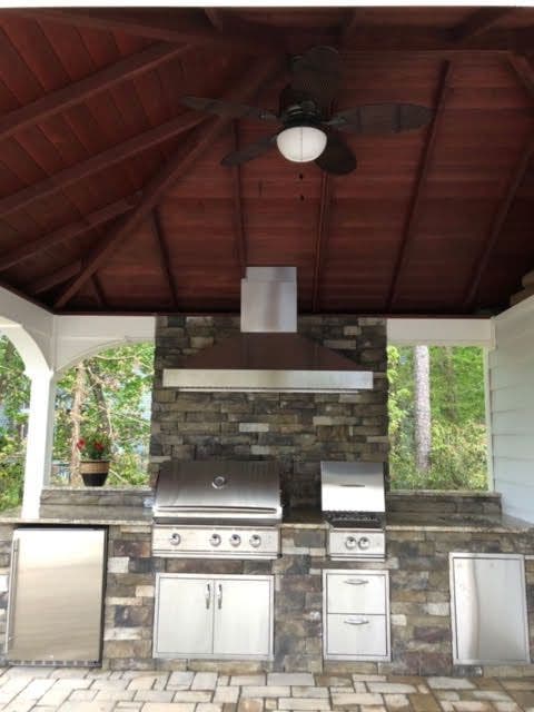 Tranquil outdoor cooking area with a Proline range hood, built-in stainless steel appliances within a stone structure, beneath a wooden gazebo - prolinerangehoods.com.