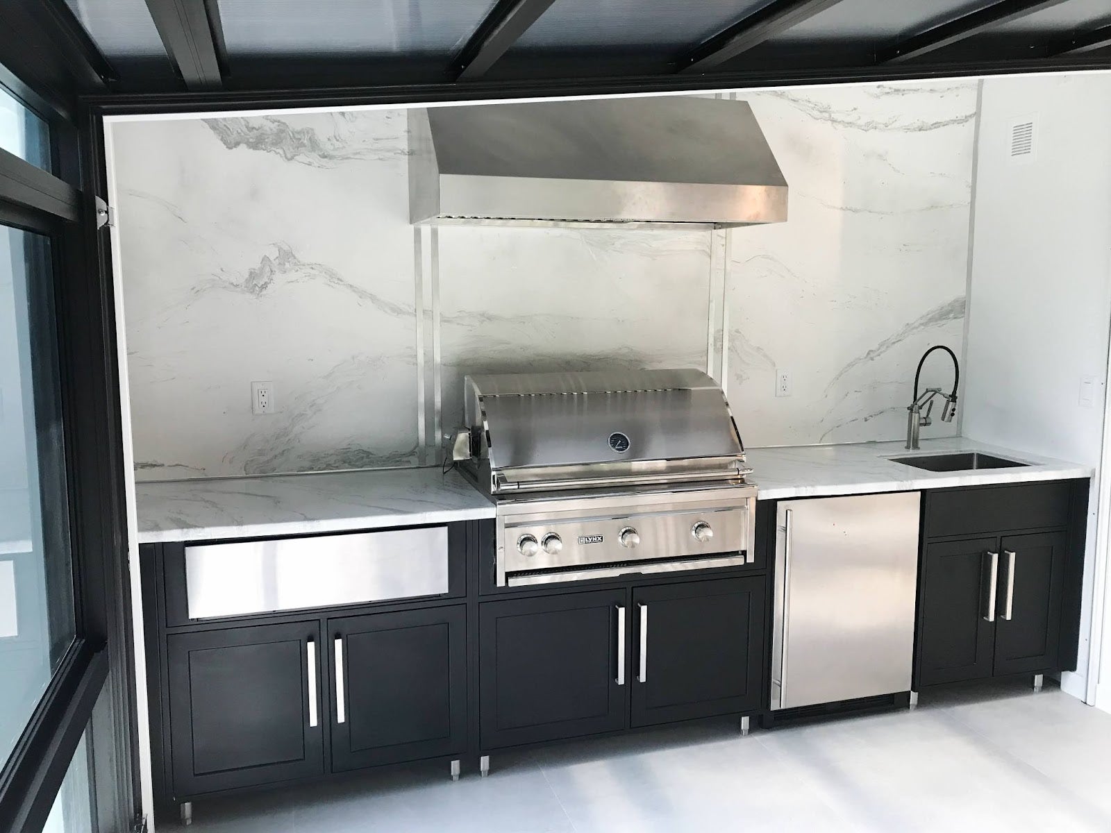 Modern indoor kitchen with a Proline range hood, featuring marble walls and black cabinetry, reflecting an elegant monochromatic design - prolinerangehoods.com