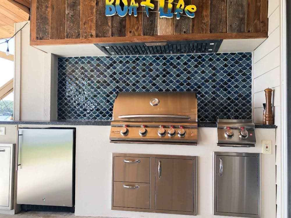 Sleek Proline range hood installed in a modern outdoor patio kitchen with fish scale backsplash tiles, surrounded by stainless steel cabinetry and a wooden overhang - prolinerangehoods.com