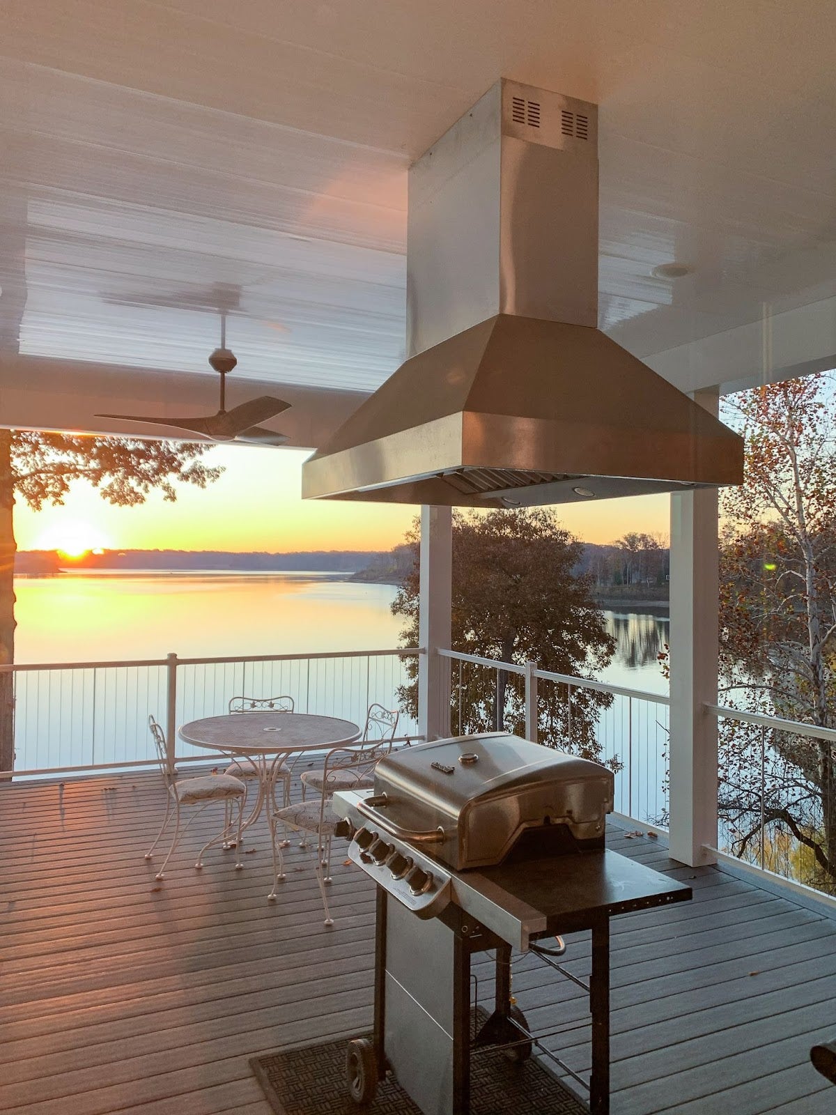 Serene deck kitchen with modern grilling amenities overlooking a tranquil lake at dusk. - Proline Range Hoods - prolinerangehoods.com 
