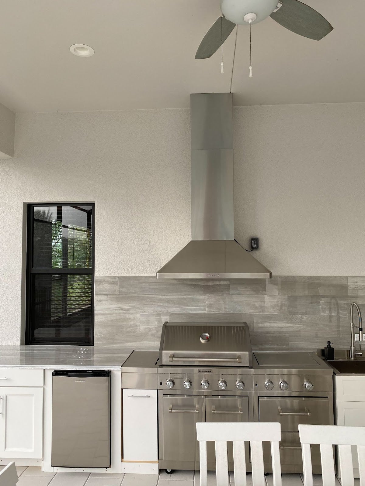 Minimalist covered patio kitchen with a stainless steel Proline range hood, white cabinetry, and a contemporary dining area - prolinerangehoods.com