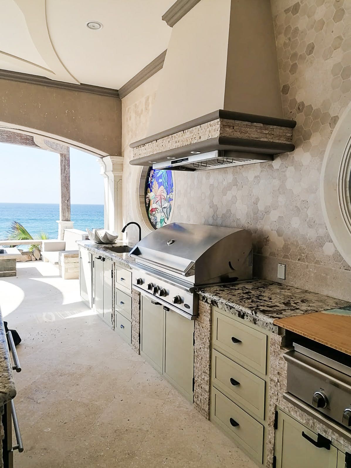 Luxurious beachfront outdoor kitchen with a Proline range hood, mosaic tile wall, and panoramic ocean views - prolinerangehoods.com