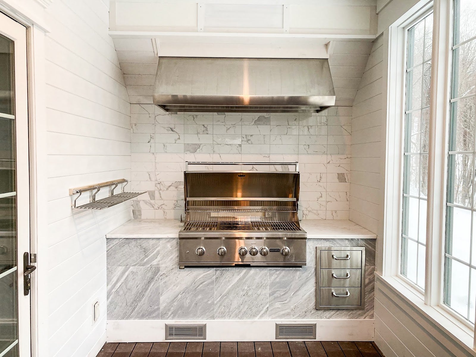 Luxurious indoor/outdoor white marble kitchen with a sleek Proline range hood and high-end grill, offering a clean and sophisticated cooking space - prolinerangehoods.com.