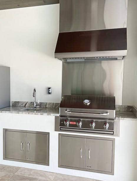 Sleek outdoor kitchen featuring a Proline range hood, built-in grill, and gray storage cabinets with a marble countertop - prolinerangehoods.com