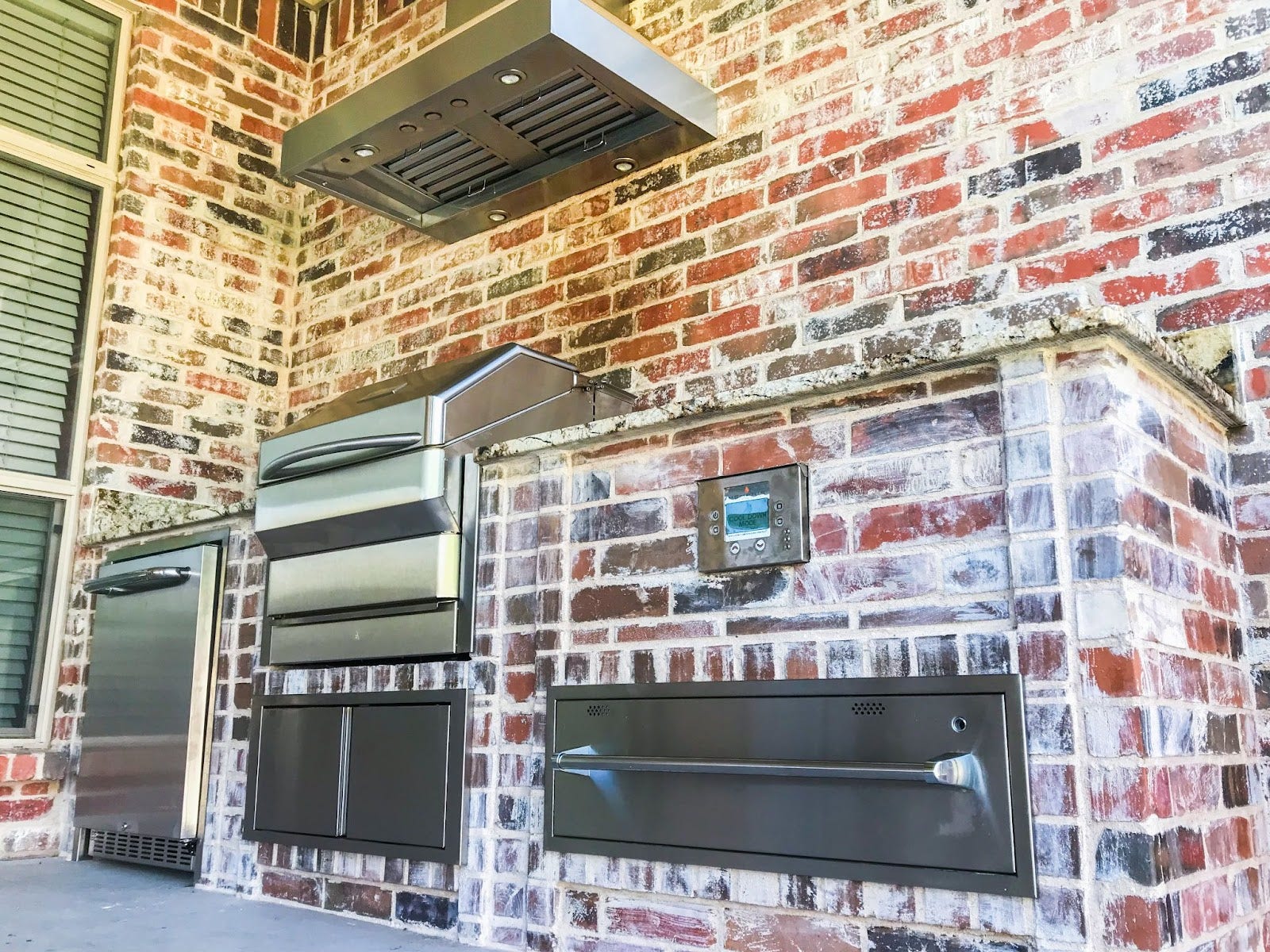 Spacious patio cooking area featuring a stainless steel Proline range hood against a multi-colored brick backdrop - prolinerangehoods.com