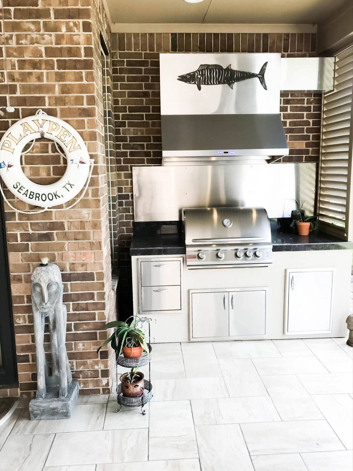 Proline range hood installed in a cozy corner outdoor kitchen with nautical decor and a fish wall art - prolinerangehoods.com