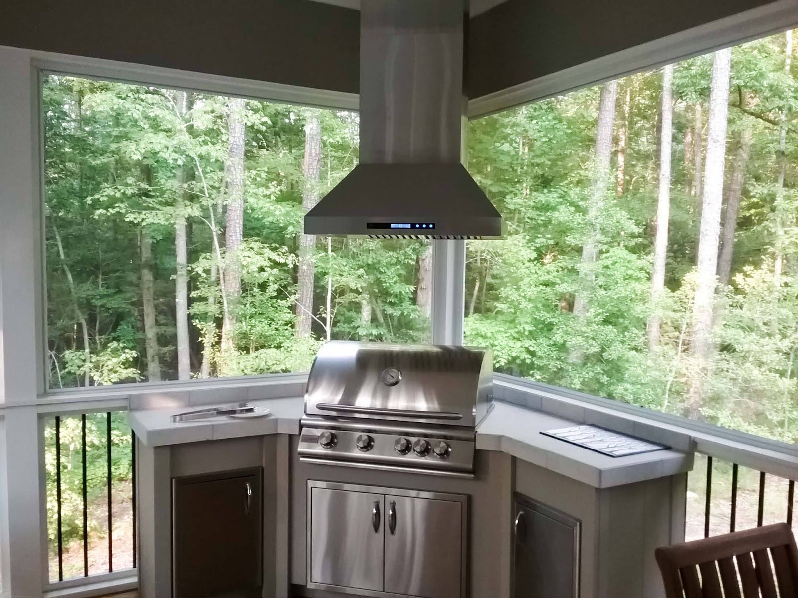 Forest-view kitchen on an enclosed patio featuring a high-end barbecue grill and sleek vent hood, perfect for nature-inspired dining.