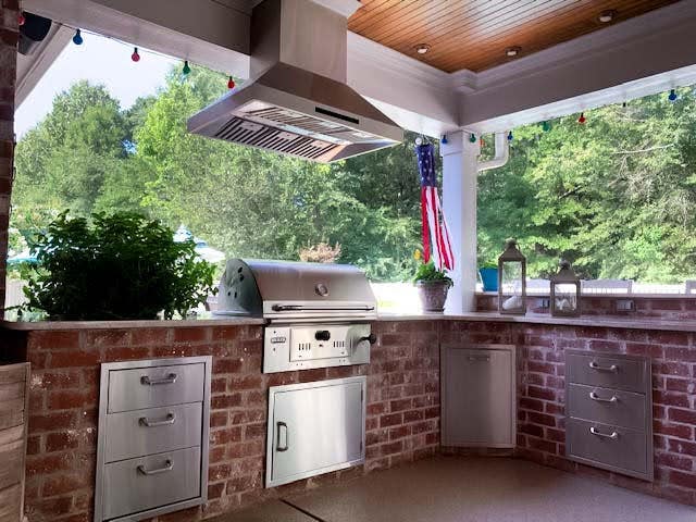 Inviting patio grill station with a brick facade, featuring a modern barbecue and ventilation hood, complemented by patriotic decor and greenery.