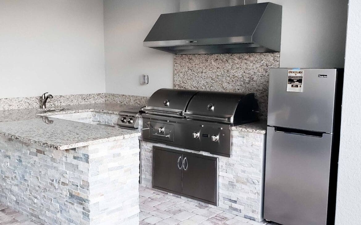 Modern outdoor kitchen setup with a Proline range hood, dual barbecue grills, and granite worktops, complemented by stone brickwork - prolinerangehoods.com