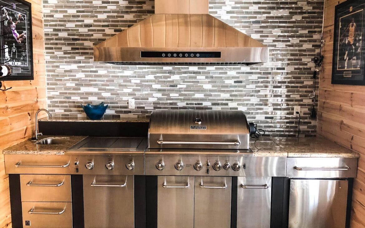 Proline outdoor range hood with advanced filtration system, perfectly complementing the stainless steel grill below for an unmatched cooking experience - learn more at prolinerangehoods.com.