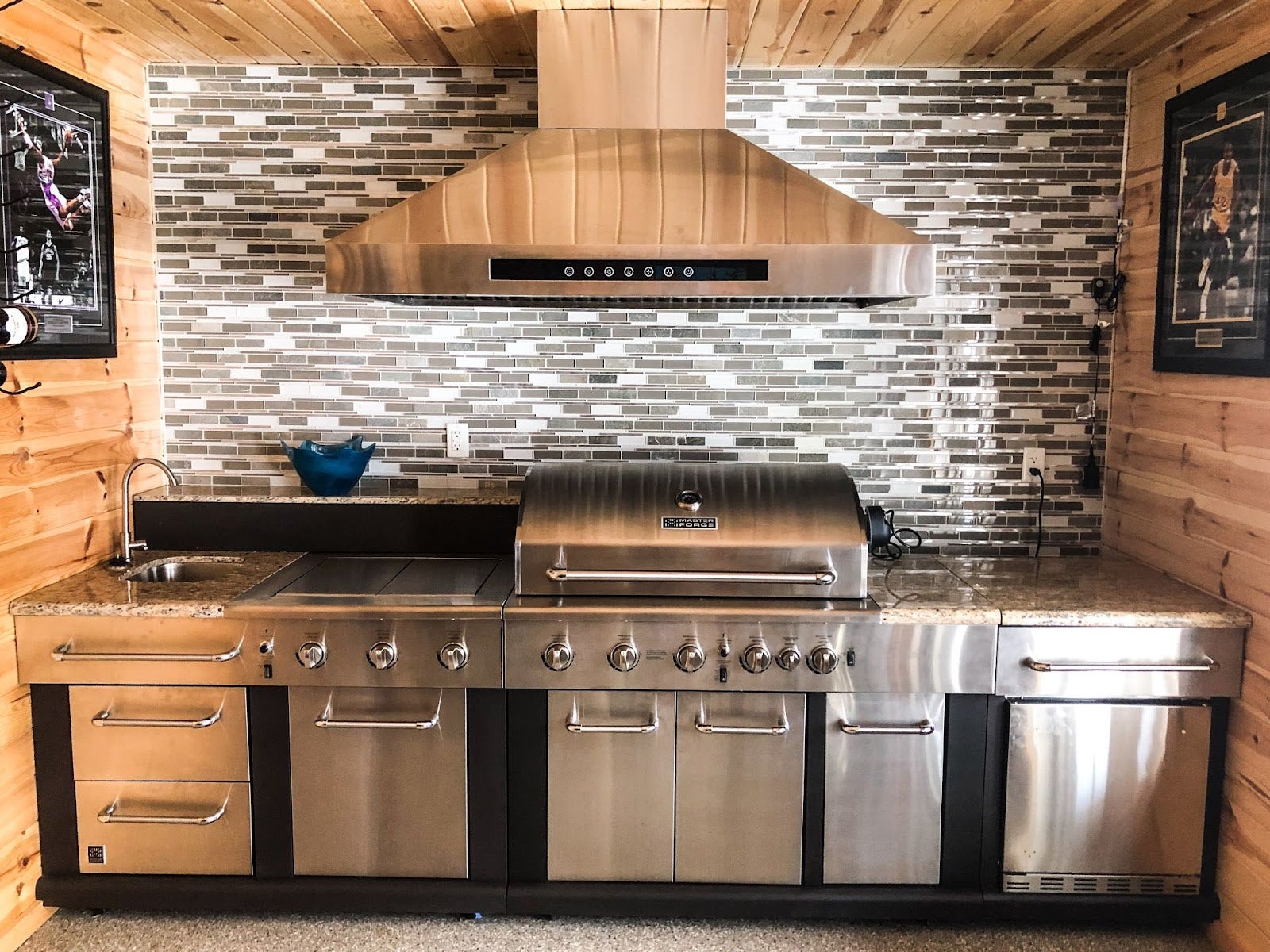 Cozy cabin outdoor cooking space featuring a Proline range hood, large stainless steel grilling station, and elegant backsplash design - prolinerangehoods.com