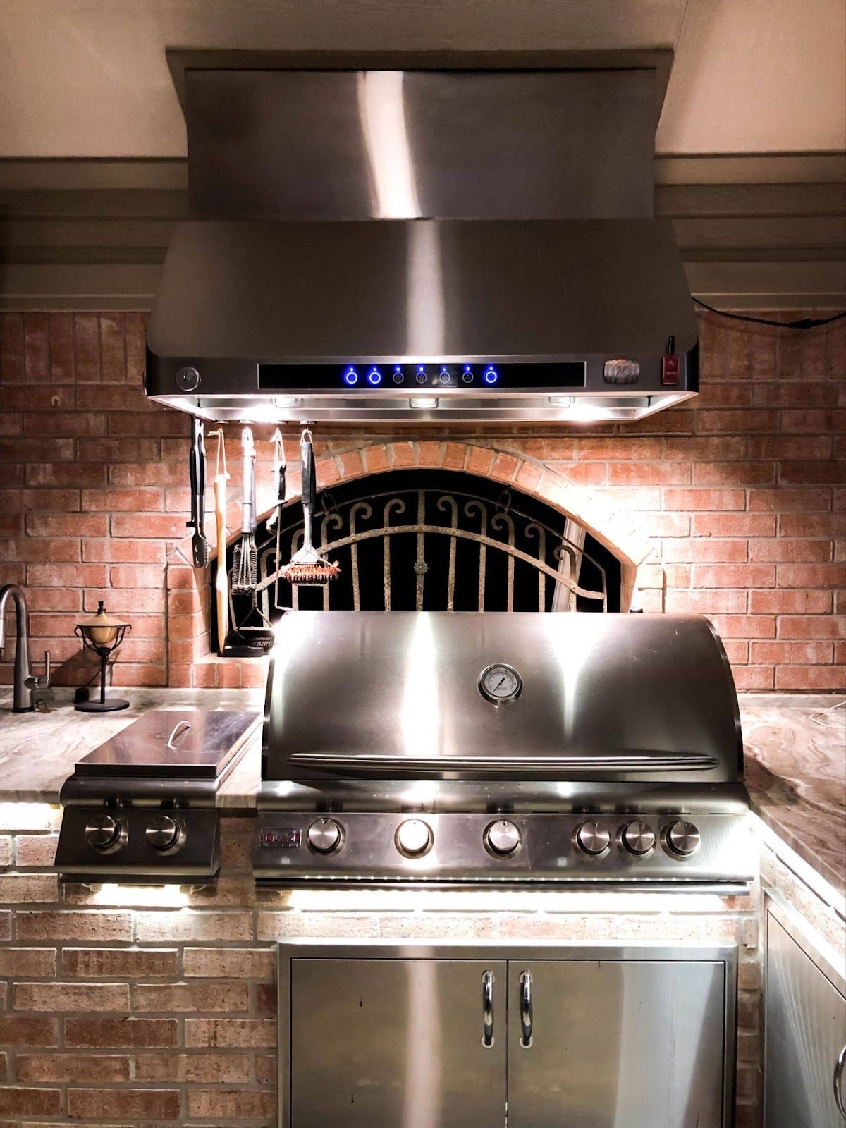 Traditional brick surround indoor grilling station with illuminated Proline range hood and stainless steel barbecue - prolinerangehoods.com