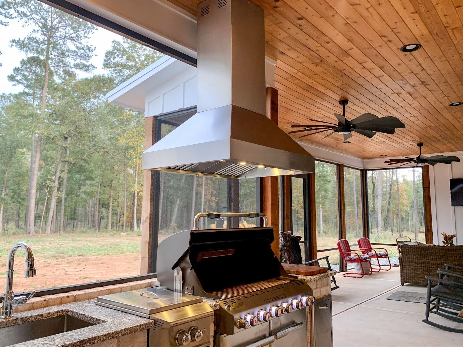 Tranquil outdoor entertainment area featuring a high-end grill, wood ceiling, and panoramic views of a pine forest.