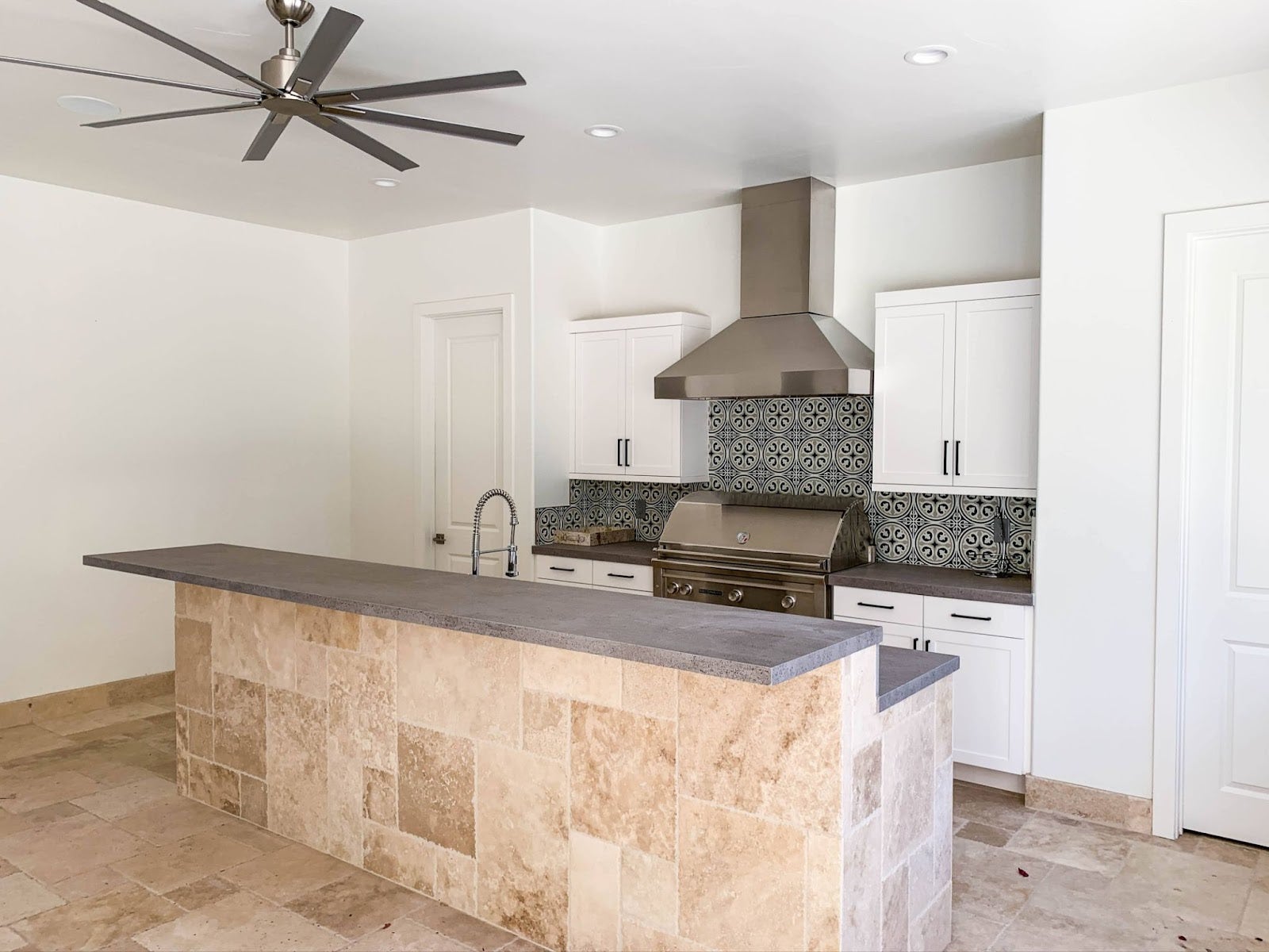 Airy kitchen interior with high ceilings, complete with a Proline range hood, contrasting patterned backsplash, and an elegant island with seating space - prolinerangehoods.com.