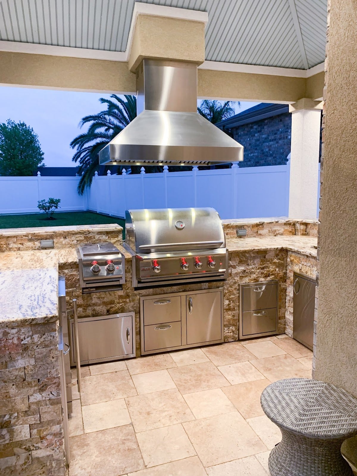 Proline range hood in an elegant outdoor kitchen with stone accents under a covered patio - prolinerangehoods.com