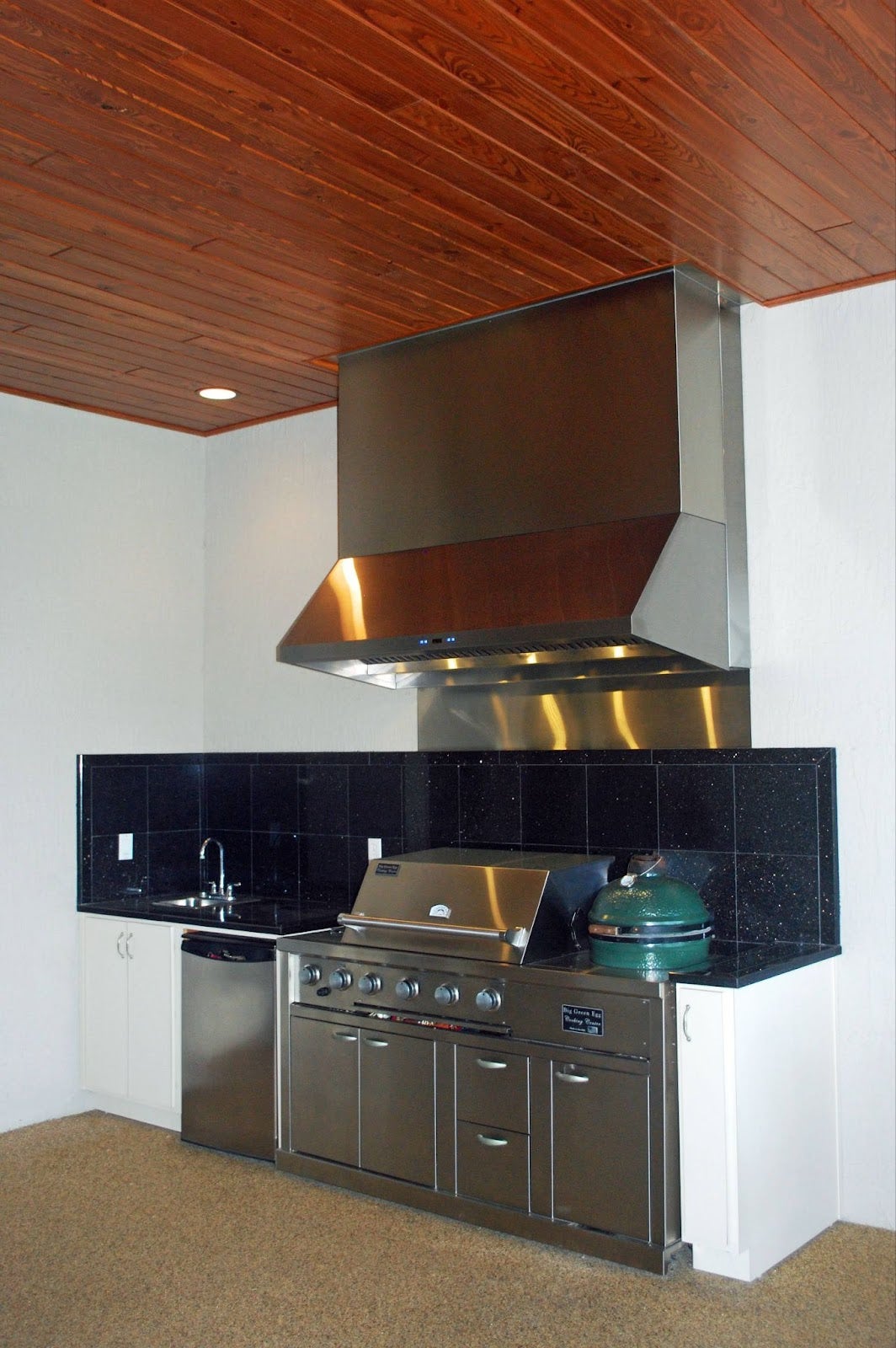 Modern home grilling station featuring a Proline range hood, stainless steel appliances, and dark countertops, with a warm wooden ceiling for contrast - prolinerangehoods.com.