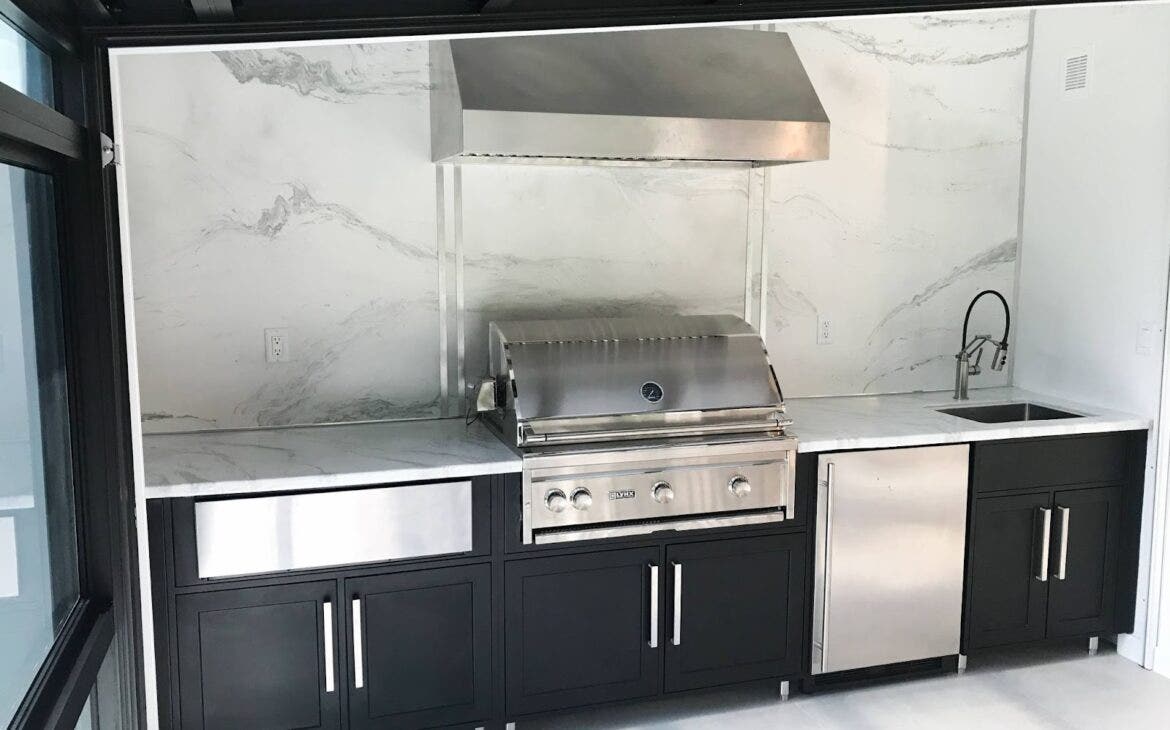 Impressive Proline outdoor range hood towering over a fully equipped stainless steel grill, set against a backdrop of natural beauty - see more at prolinerangehoods.com.