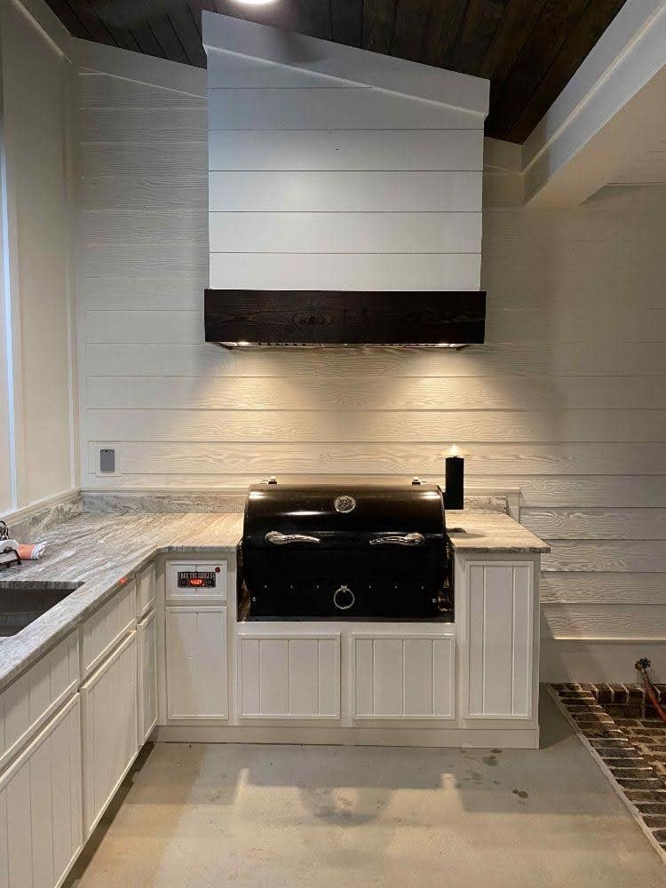 Stylish white kitchen featuring a sleek Proline range hood, paired with a classic black barbecue grill and elegant marble counters, creating a clean and inviting cooking space - prolinerangehoods.com