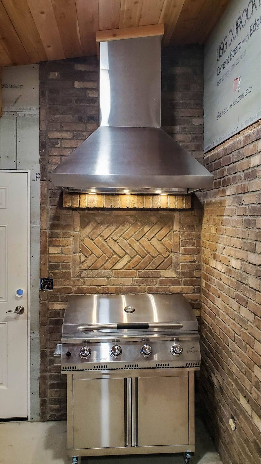 Rustic indoor grilling space highlighted by a stainless steel Proline range hood against a brick wall, merging industrial style with homely warmth - prolinerangehoods.com.
