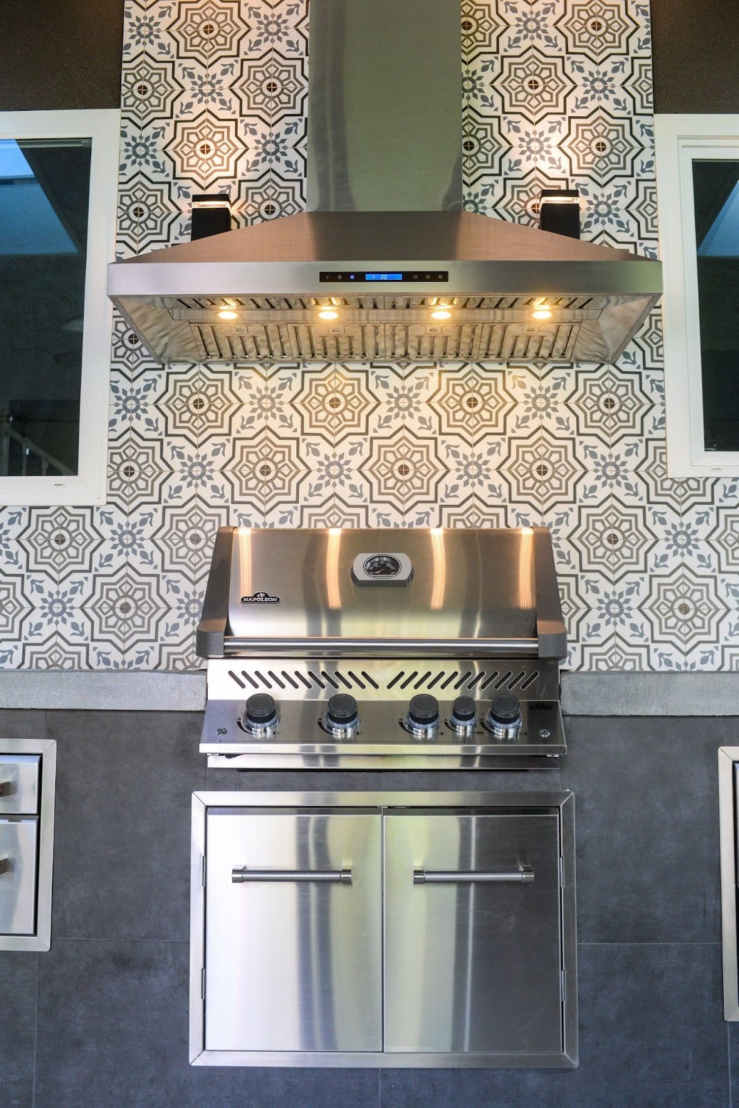 Striking Proline range hood over a stainless steel grill, showcased in a modern outdoor kitchen with intricate patterned wall tiles - prolinerangehoods.com.
